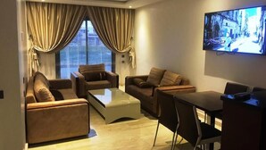 Uma sala de estar moderna com uma televisão de tela plana na parede, uma mesa de jantar com cadeiras e dois sofás.
