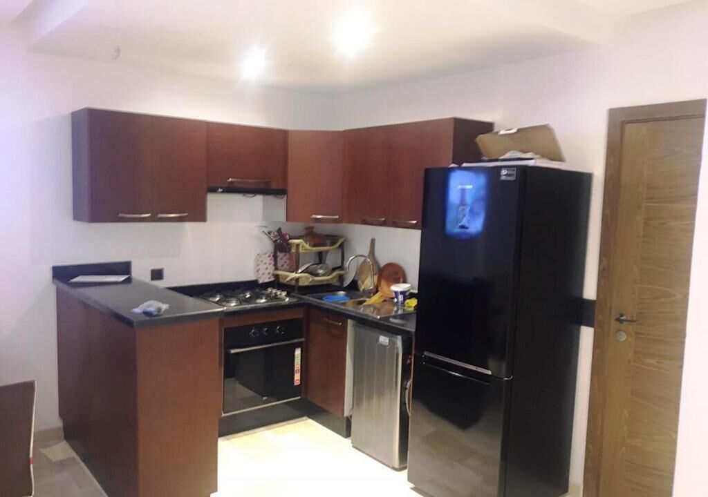 Uma cozinha compacta com armários de madeira escura, geladeira preta, fogão e lava-louças.