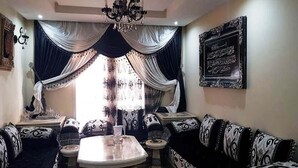 Een woonkamer met een ronde salontafel, zwart-wit gestreepte banken, een kroonluchter en een groot raam met gordijnen.
