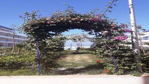 An outdoor garden area with a floral archway, a pathway, and a view of a building in the background. - Residence Adan Beach 4724 (Aourir)