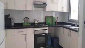 Una cocina con armarios blancos, encimera negra, estufa, horno y microondas, además de una ventana.
