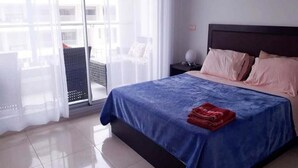 A hotel room with a large bed, a nightstand, a chair, and a view through a glass door. - Residence Adan Beach 4790 (Aourir)