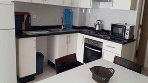 A compact kitchen with white cabinets, a black countertop, a microwave, a stove, and a sink. - Residence Adan Beach 4790 (Aourir)