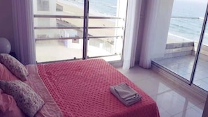 Een slaapkamer met een groot bed, uitzicht op de oceaan vanaf een balkon, en een betegelde vloer.