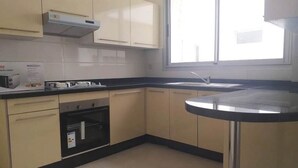 Cucina con mobili color beige, piano di lavoro nero, forno integrato e finestra che lascia entrare luce naturale.