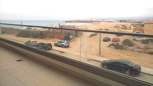 Vista da un balcone su una spiaggia, con auto parcheggiate e una costa in lontananza.
