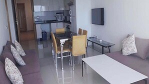A modern living room with a sofa, a dining table, and a kitchen in the background. - Residence Adan Beach 4803 (Aourir)