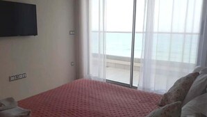 A bedroom with a pink bedspread, a flat-screen TV mounted on the wall, and a large window with a view of the beach. - Residence Adan Beach 4803 (Aourir)