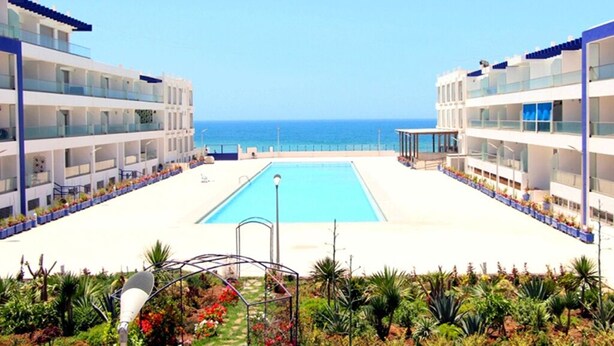 A hotel with a central pool, multiple balconies, and a view of the sea.