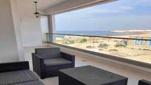 A balcony with wicker furniture, a view of the beach, and a clear sky.