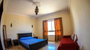 Une chambre à coucher avec un lit, une table de chevet, un canapé rouge, une fenêtre avec des rideaux et un luminaire au plafond.