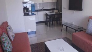 A living room with a sofa, a coffee table, and a TV. There is a kitchen in the background with a dining table and chairs. - Residence Adan Beach 4786 (Aourir)