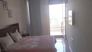 A bedroom with a bed, a nightstand, a TV, and a view of the outdoors. - Residence Adan Beach 4786 (Aourir)