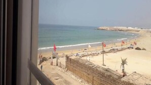 Vue sur la plage depuis l’intérieur d’un bâtiment, avec une plage de sable, l’océan et un promontoire rocheux au loin.