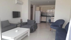 Un salon moderne avec un canapé gris, une table basse blanche et un fauteuil bleu. Un téléviseur à écran plat est fixé au mur.