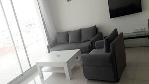 Un salon moderne avec un canapé d’angle gris, une table basse blanche et un téléviseur à écran plat fixé au mur.