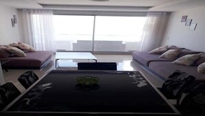 A modern living room with a glass-top table, two sofas, and a large window with curtains. - Residence Adan Beach 4802 (Aourir)