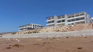 A coastal hotel with multiple floors, a rocky shoreline, and clear skies. - Residence Adan Beach 4802 (Aourir)