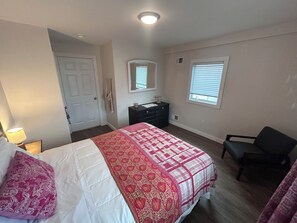 A bedroom with a bed, dresser, chair, and a window with blinds.