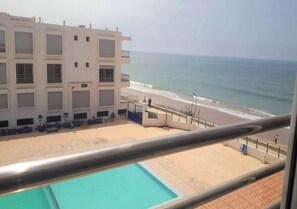 A hotel with a pool, beach view, and a building with multiple balconies.