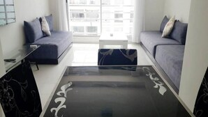 Een moderne woonkamer met een glazen salontafel, twee grijze banken en een witte bijzettafel.