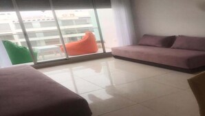 Ein modernes Wohnzimmer mit einer Couch, einem Sessel und einem Balkon mit Blick auf Gebäude.