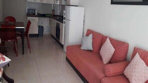 Un espacio habitable compacto con kitchenette, comedor y sofá con cojines estampados.