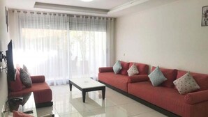 Ein Wohnzimmer mit einem roten Sofa, einem weißen Couchtisch und einem Fernseher auf einem Schrank.