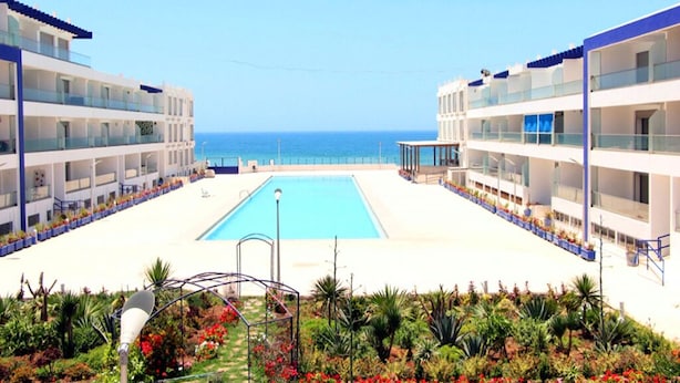 Un hotel con piscina central, varios balcones y vista al mar.