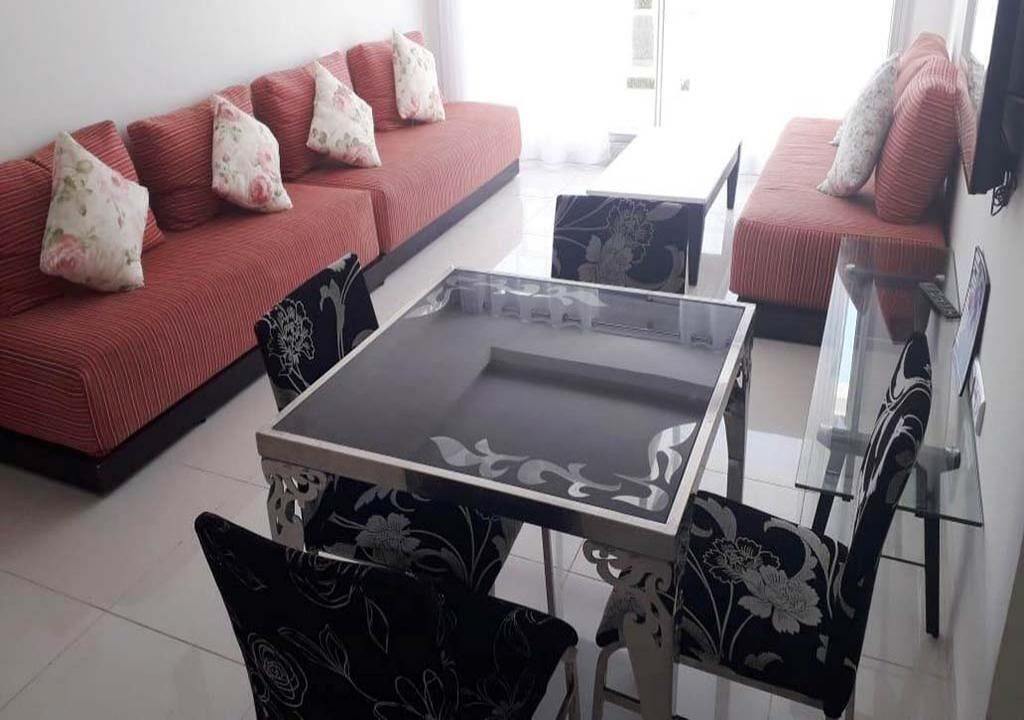 A living room with a glass-top coffee table, two sofas with floral cushions, and patterned chairs.