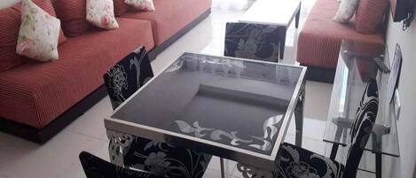 A living room with a glass-top coffee table, two sofas with floral cushions, and patterned chairs.