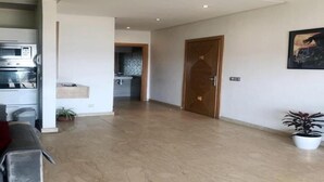 Amplia sala de estar con cocina al fondo, una puerta de madera y una planta en maceta.