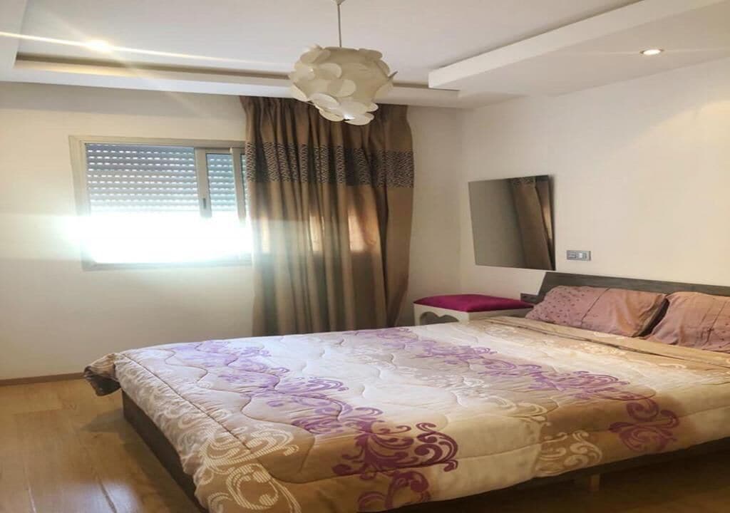 A bedroom with a bed, a bedside table, a mirror, and a window with curtains.
