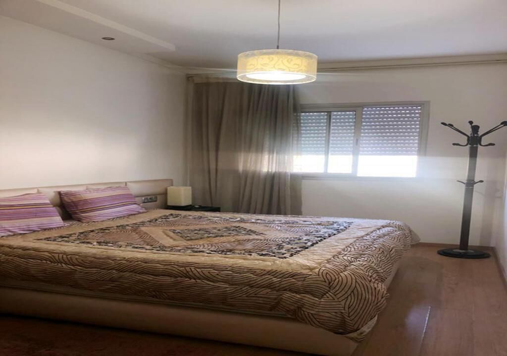 A bedroom with a large bed, a bedside lamp, a window with blinds, and a floor lamp.