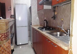 A compact kitchen with a refrigerator, stove, sink, and wooden cabinets. - Residence Caprice Palace 4826 (Marrakech)