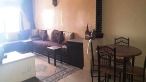 Een woonkamer met een bank, een eettafel met stoelen, een kamerkleed met een patroon en een decoratieve lantaarn.