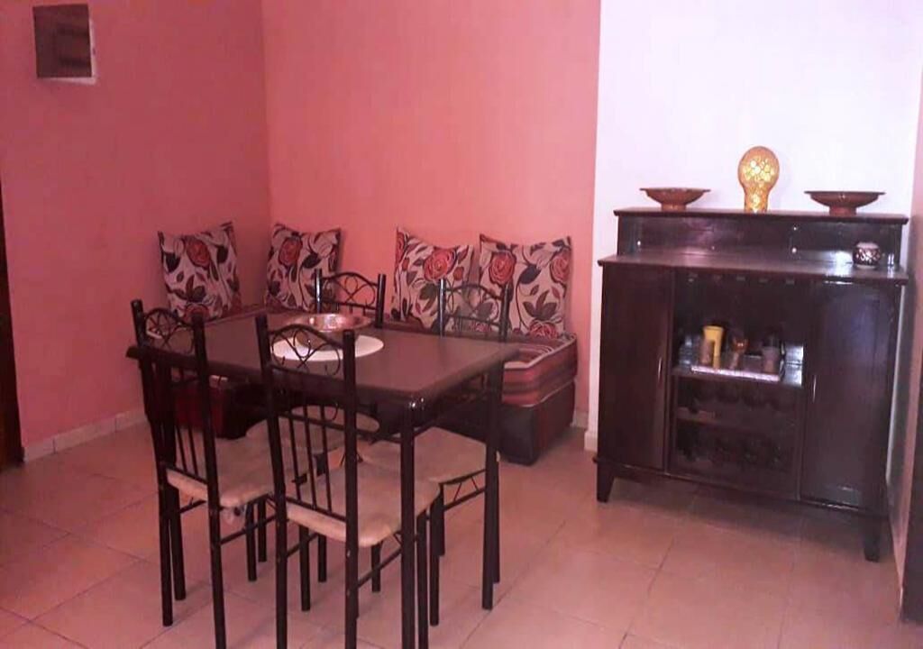 A dining area with a table and chairs, a sofa with patterned cushions, and a cabinet with decorative items.