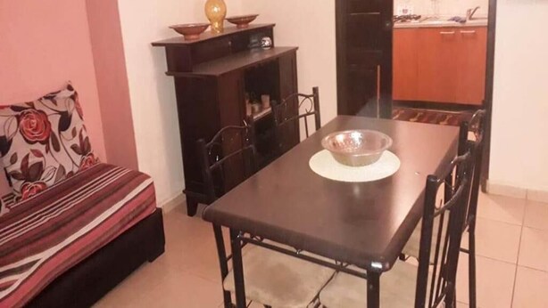 A compact living space with a dining table and chairs, a sofa, a small cabinet, and a kitchen area visible through an open door.