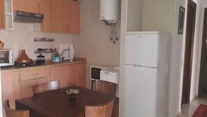 Cocina compacta con armarios de madera, refrigerador blanco, estufa y una mesa de comedor con sillas.