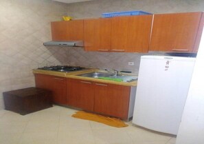 A kitchen with wooden cabinets, a gas stove, a sink, and a white refrigerator. - Residence Caprice Palace 4846 (Marrakech)