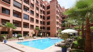 Ein mehrstöckiges Hotel mit Schwimmbad, Außenbereich und Palmen.