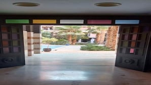Ein offenes Durchgangstor, das in einen Innenhof mit Pool, Palmen und einem Gebäude im Hintergrund führt.