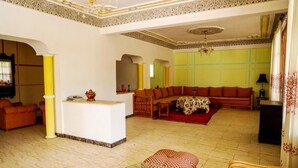 Ein geräumiges Wohnzimmer mit einer Sofagarnitur, einem Couchtisch und einem kleinen Tisch mit Dekoration. Eine gelbe Säule und ein Kronleuchter sind ebenfalls vorhanden.