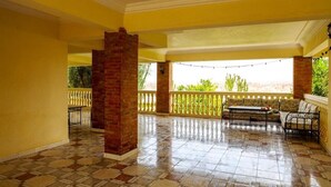 Ein überdachter Patio-Bereich mit Fliesenboden, einer Ziegelstütze, einer Couch und einem Geländer.