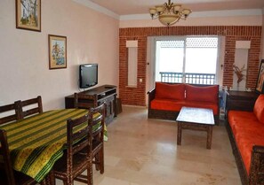 A living room with a sofa, a dining table with chairs, a television, and a balcony with a view. - Marina Agadir Residence 4903 (Agadir)