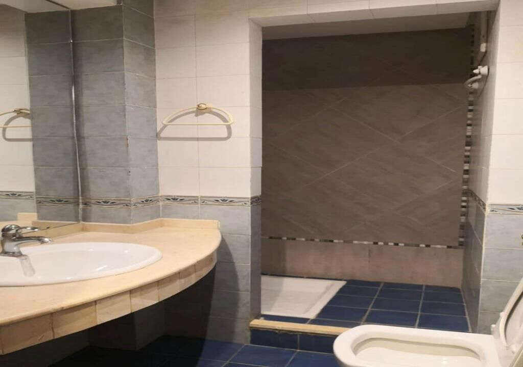 A bathroom with a sink, mirror, towel rack, shower, and toilet.