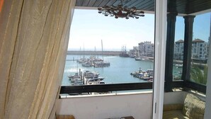 Un balcon donnant sur un port de plaisance, un canapé, une petite table et un luminaire suspendu.