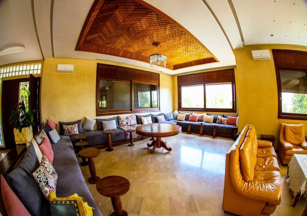 A spacious living area with a high ceiling, large windows, and a central round table.