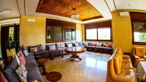 A spacious living area with a high ceiling, large windows, and a central round table. - Sublime Villa with swimming pool in Illigh Agadir 4906 (Agadir)
