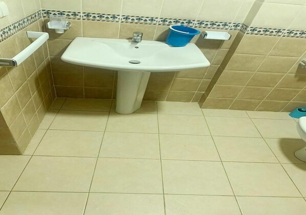 A bathroom with a white sink, beige tiles, and a blue bucket on the wall. - Residence Kabila Vista 4924 (Mdiq)